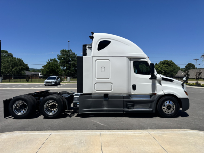Freightliner Cascadia 126 sleeper cab tractor in a parking lot, side profile view showing the tractor’s cab, fuel tanks, and rear axles.