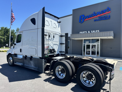 Truck in front of Bruckners Truck & Equipment building with Freightliner semi-truck cab, white, showing tandem rear axles and fifth wheel. Visible text on truck cab and rear: number 016, chrome wheels, black chassis. Building signage reads 