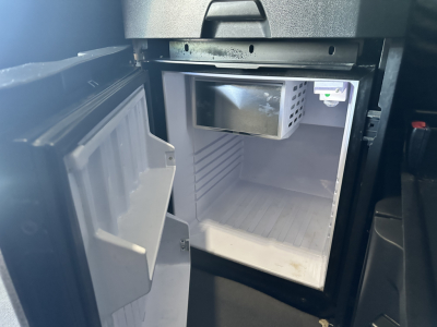 Freightliner Cascadia 126 sleeper truck interior showing a small under-dash cooler/freezer with open door and empty fridge compartment.