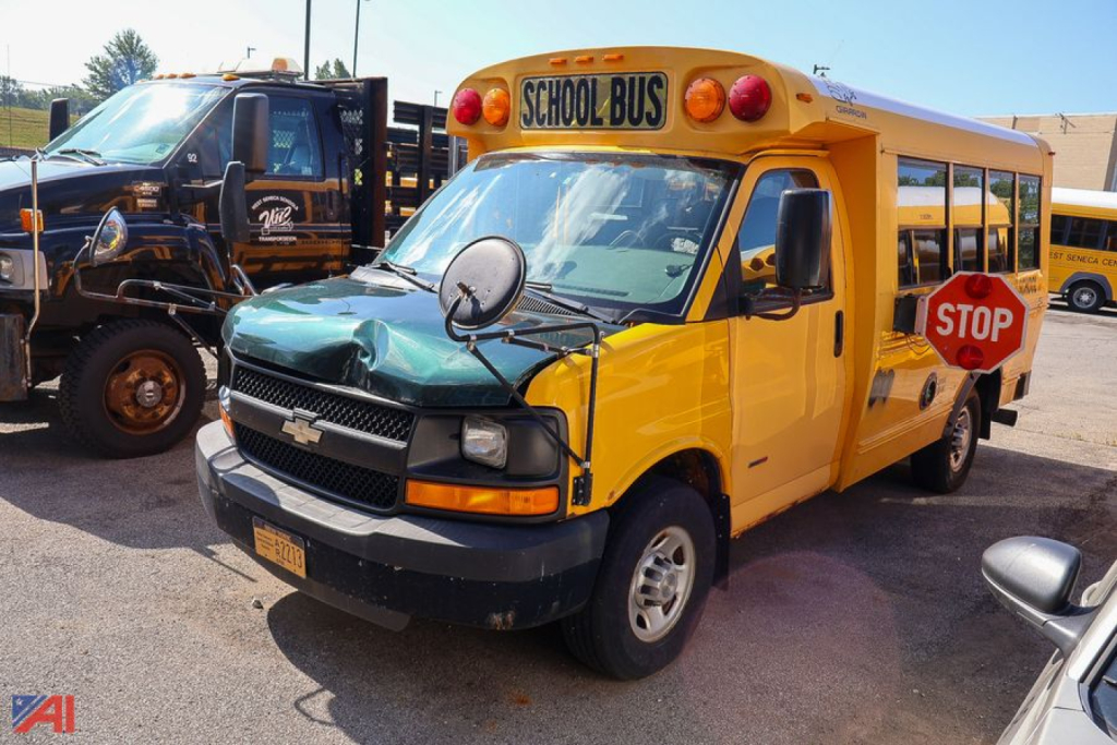 Yellow school bus with 'SCHOOL BUS' sign on top, front hood green, stop sign extended on side, Chevrolet logo, bus mirrors, and surrounding vehicles.