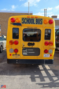 Rear view of a yellow Chevrolet Express school bus with 'SCHOOL BUS' sign, emergency door, and multiple red/amber lights.