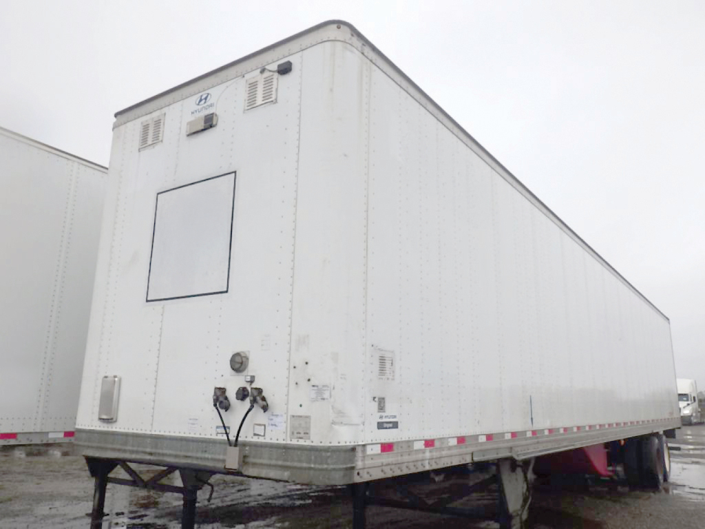 Trailer rear view showing mounted Hyundai logo, plumbing and utility panels, with doors and light fixtures on a white cargo trailer.