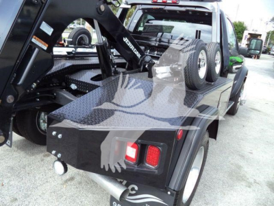 Ram 4500 SLT flatbed tow truck with dual rear wheels and winch equipment on a black utility bed, showing taillights, exhaust, and toolbox.