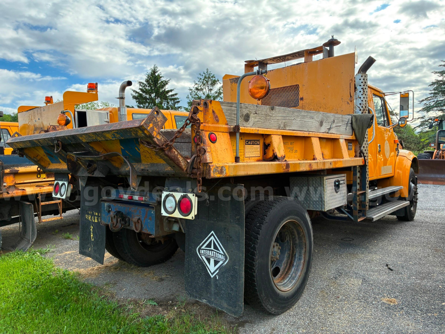 Dump truck rear view showing hydraulic bed and taillights with black mud flaps and reflective triangles.