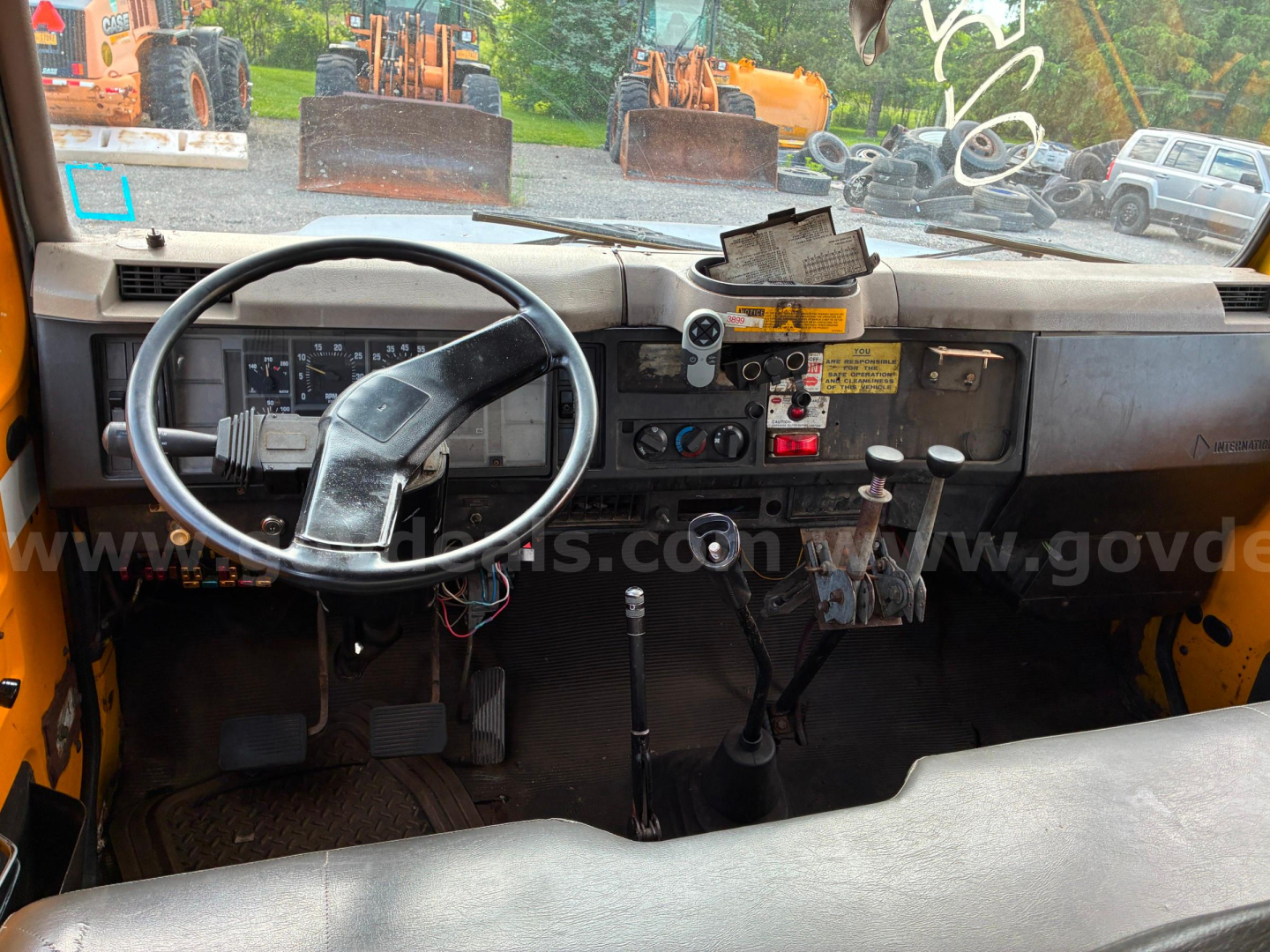 Dump truck cab interior view with steering wheel and dashboard showing gauges and controls.