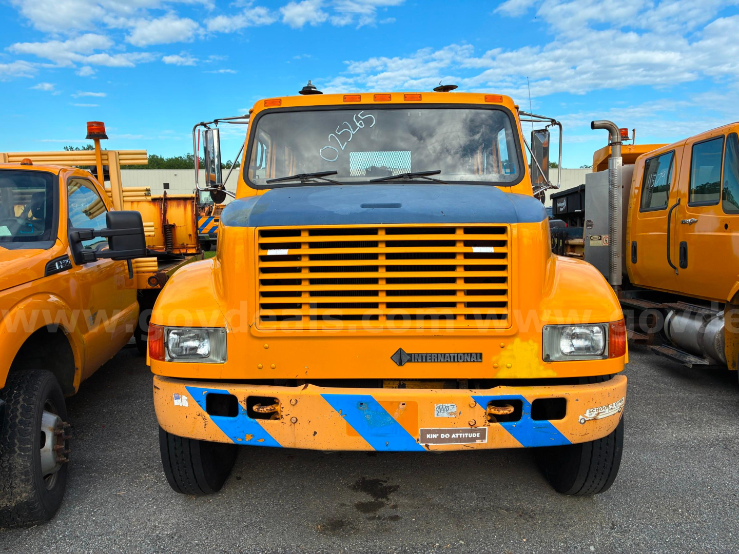 International 4700 dump truck front view showing large grille, orange cab, and blue diagonal safety stripes on the bumper.