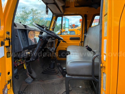 Truck cab interior of a 2002 International 4700 dump truck showing steering wheel, dashboard, and bench seat.