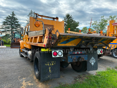 Dump truck bed of a used 2002 International 4700 in a lot, rear view with yellow paint and black mud flaps.