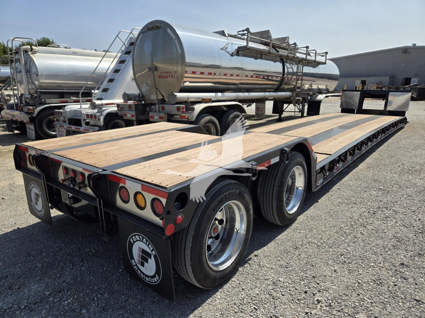 Fontaine Renegade X20 trailer with flatbed and dual rear axles, wood deck, and metal tank trailer in background.