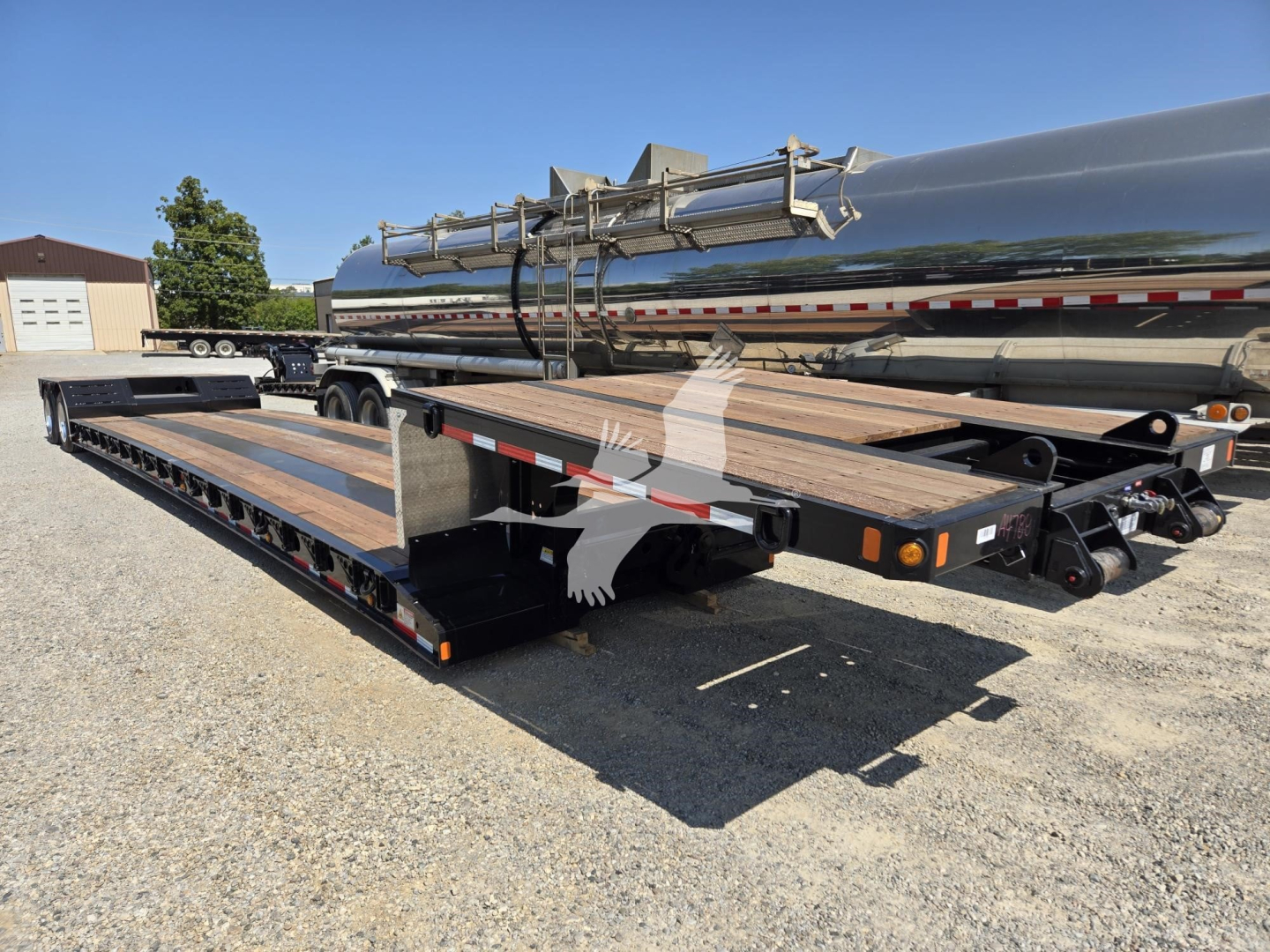 Fontaine Renegade X20 trailer with a long flatbed and a tanker-style cylindrical tank on a dual-axle trailer. Visible are wooden deck planks, metal guard rails, and a load of piping equipment. Serial/stock labels not legible.
