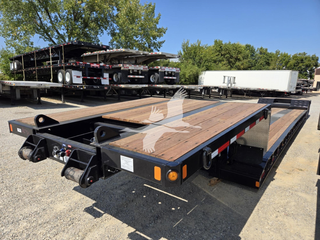 Fontaine Renegade X20 trailer flatbed in yard showing wooden deck, dual axles, and ramp storage with sticker labels.