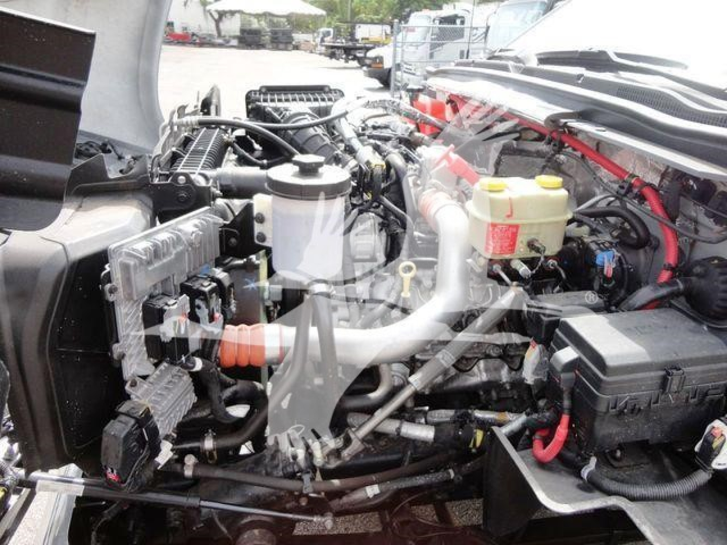 Truck engine bay view showing coolant reservoir, brake fluid reservoir, battery, hoses, and various engine components in Silverado 6500HD flatbed truck.