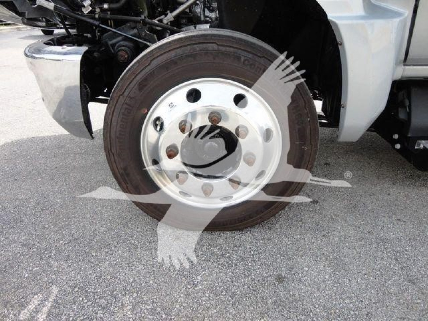 Truck wheel and hub showing steel rim with lug nuts on flatbed truck, part of front suspension visible.