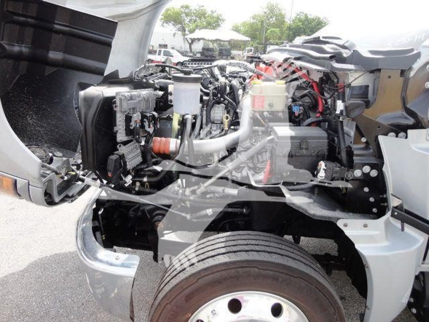Chevrolet Silverado 6500HD engine bay view showing front wheel, exposed engine components, and wiring harness in a flatbed truck setup.