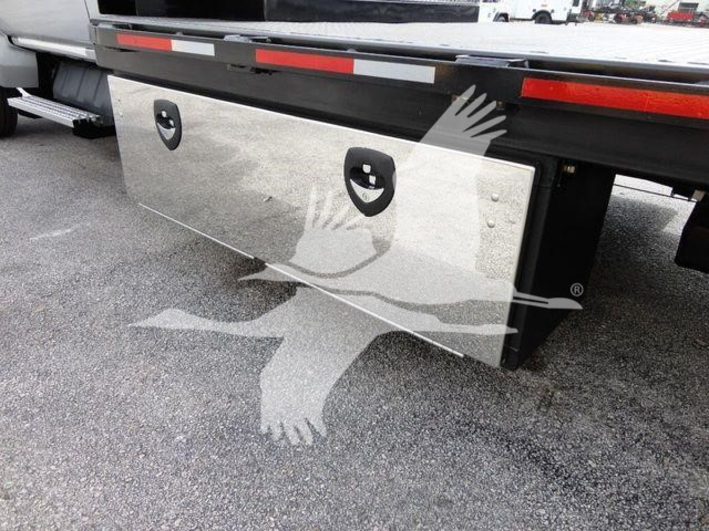 Flatbed truck rear showing a polished aluminum toolbox or plate with two circular handles and riveted joints under the Silverado 6500HD tag.