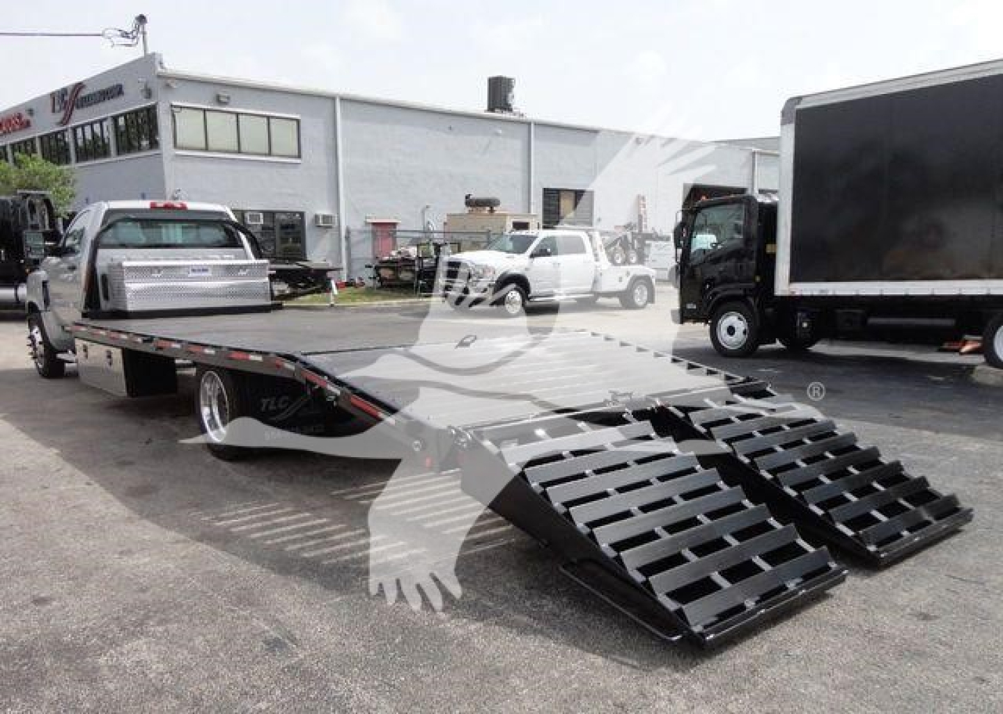 Flatbed tow truck with loading ramps extended, Chevrolet Silverado 6500HD flatbed trailer in a dealership lot.