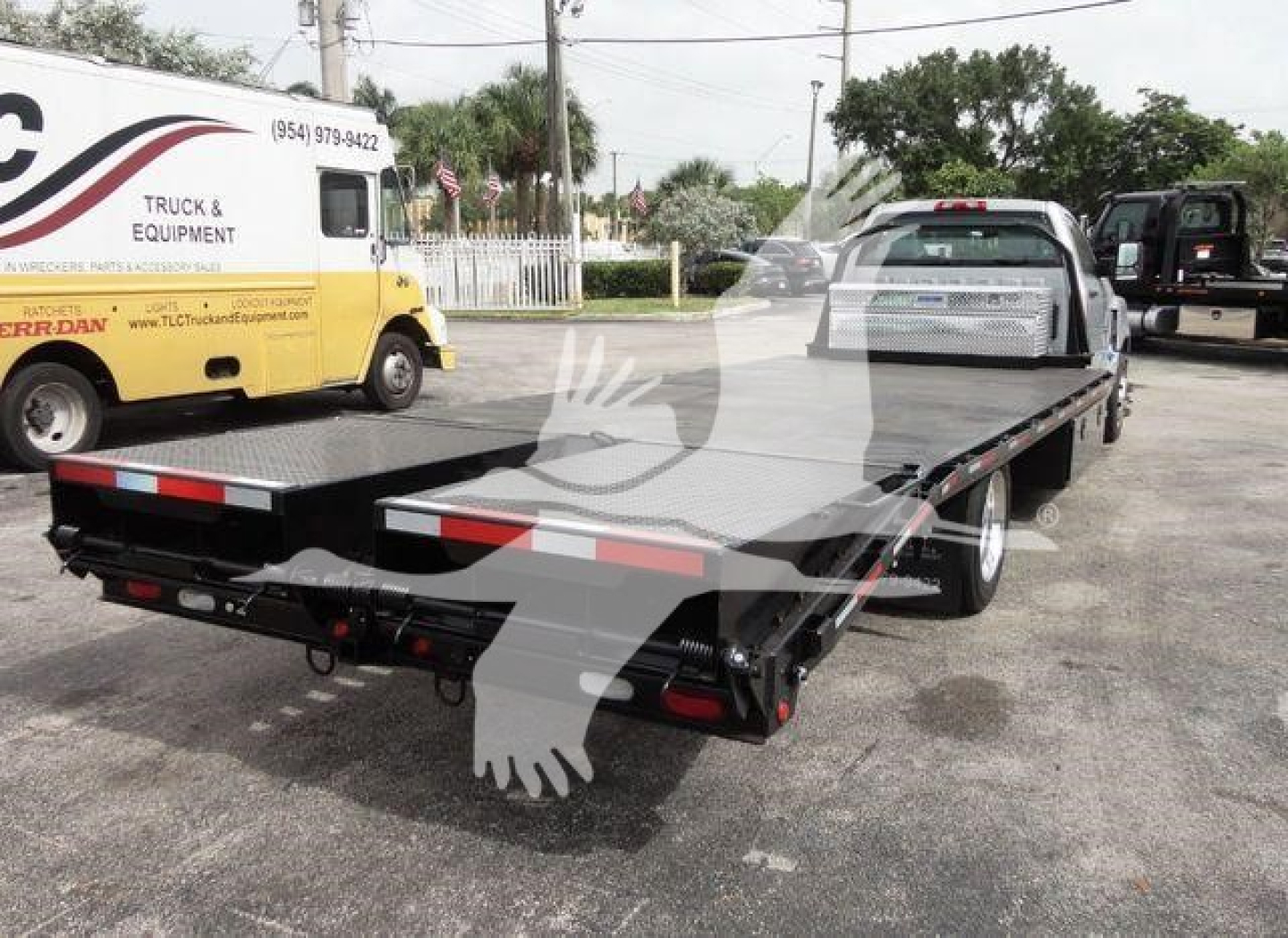 Flatbed tow truck with Chevrolet Silverado 6500HD in-service showing a dual rear wheels and flatbed, truck and equipment truck in background.