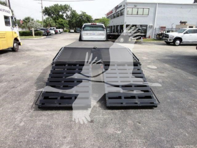 Flatbed tow truck with a low-loading ramp on a Chevrolet Silverado 6500HD chassis showing metal ramp sections and surrounding lot.
