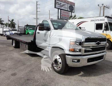 Flatbed tow truck in white 2023 Chevrolet Silverado 6500HD with long steel flatbed in a dealership lot.