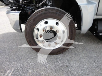 Truck wheel and hub showing steel rim with lug nuts on flatbed truck, part of front suspension visible.