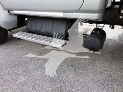 Side view of a 2023 Chevrolet Silverado 6500HD flatbed truck showing aluminum step/side step with grip surface and cylindrical fuel/air tanks under the cab.