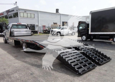 Flatbed tow truck with loading ramps extended, Chevrolet Silverado 6500HD flatbed trailer in a dealership lot.