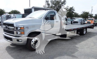 Flatbed tow truck chassis showing Chevrolet Silverado 6500HD in-service with long flatbed and dual rear wheels.