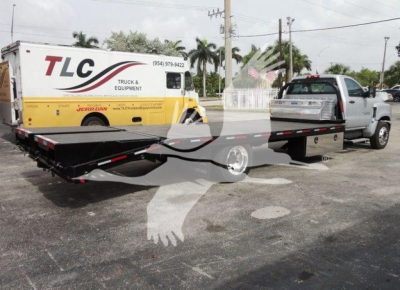 Flatbed tow truck with a long black flatbed attached to a Chevrolet Silverado 6500HD chassis, yellow TLC truck and equipment service van in background.