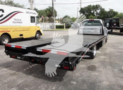 Flatbed tow truck with Chevrolet Silverado 6500HD in-service showing a dual rear wheels and flatbed, truck and equipment truck in background.