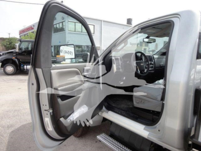 Truck cab interior showing front seats and open driver door with running board; light gray interior; dashboard and steering wheel visible; exterior silver body in background.