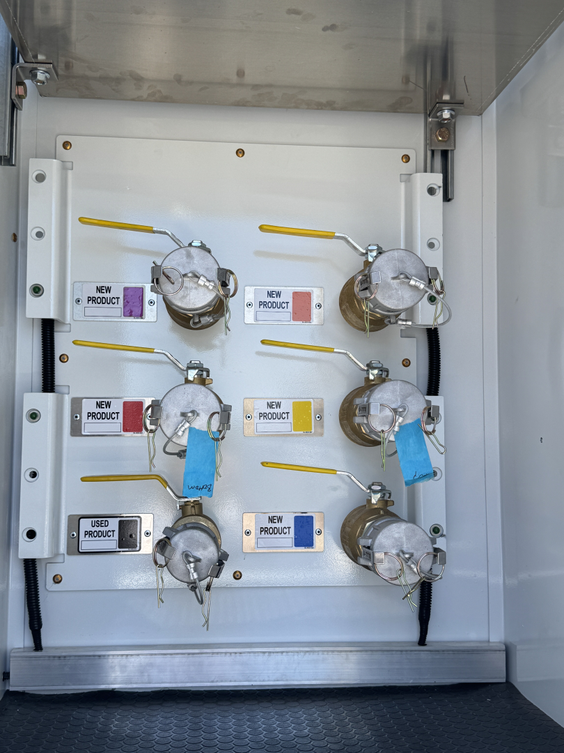 Six cylindrical gas valves with yellow handles mounted on a white panel inside a storage cabinet. Labels read NEW PRODUCT and USED PRODUCT, blue tags attached.