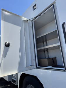 Mack MD7 service truck rear cargo compartment, open with empty shelves and interior storage racks visible.