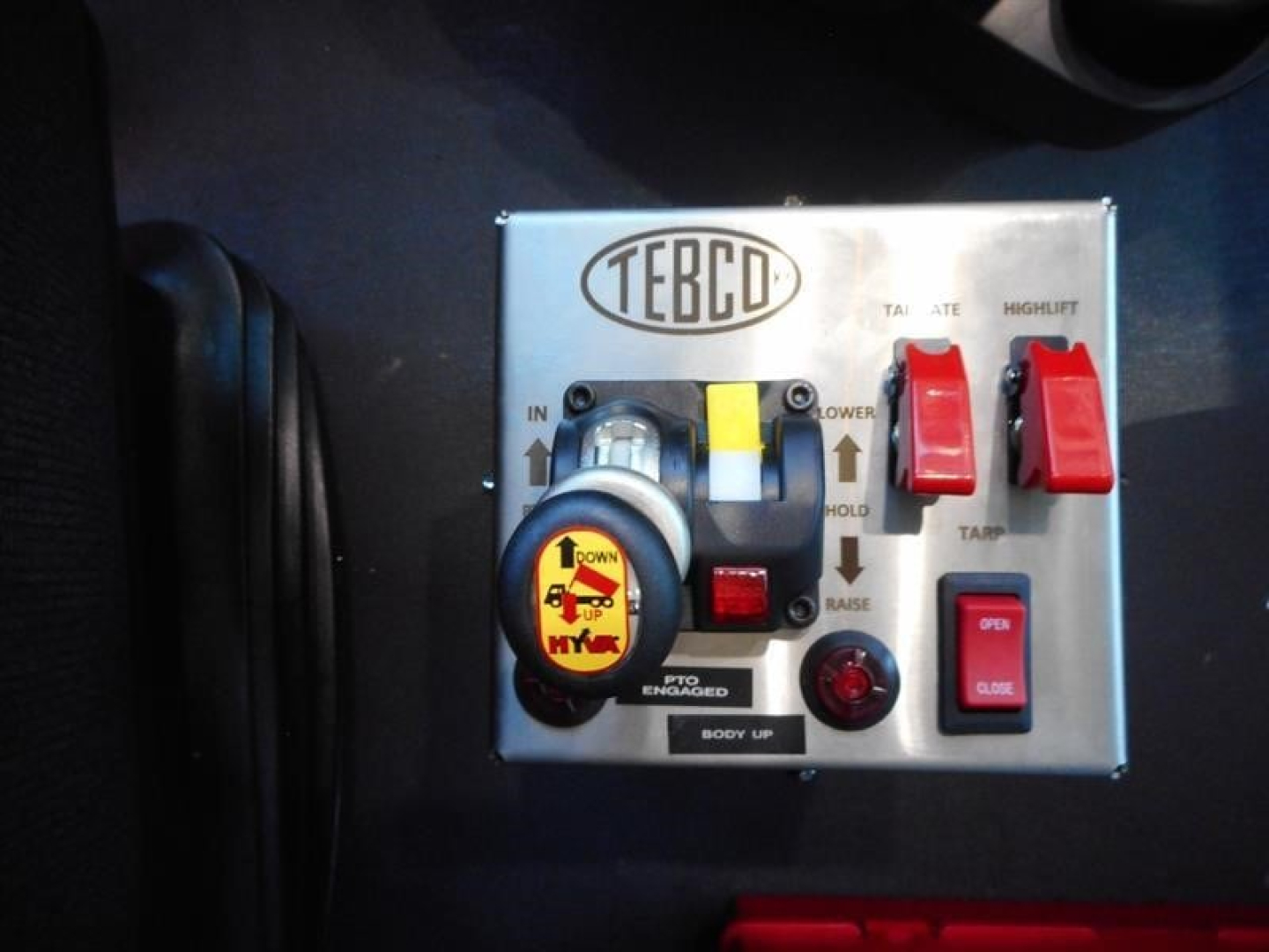 Control panel labeled TEBCO with a yellow key dial, red toggle switches, and various knobs; visible on a metallic plate.