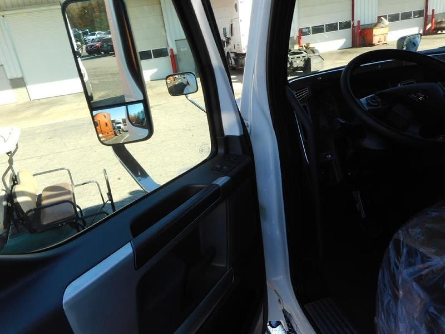 Truck cab interior view of a 2026 Western Star 47X showing open door, steering wheel, dashboard, and side mirror.