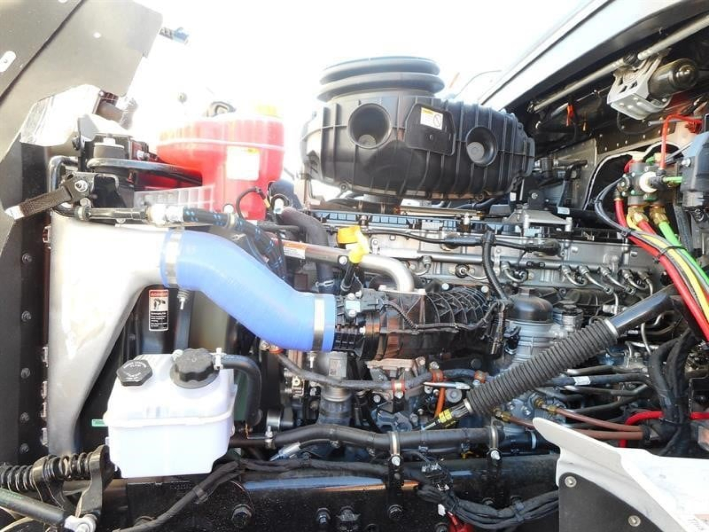 Engine bay of a 2026 Western Star 47X dump truck showing turbo intercooler hoses and fluid reservoirs with blue silicone hose in foreground.