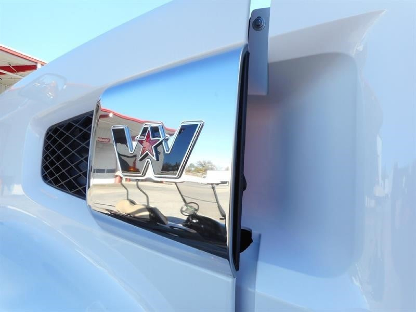 Front left hood area of a white Western Star 47X truck with chrome emblem and MV logo, showing the grille and side intake.