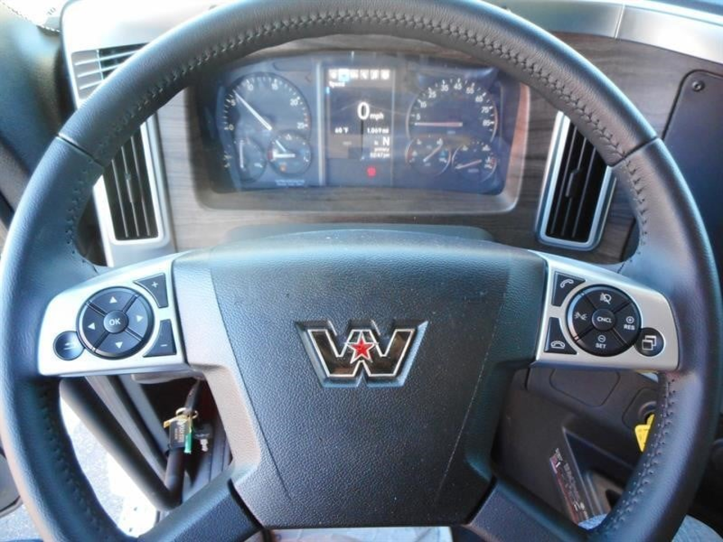 Driver's view of a Western Star truck steering wheel with dashboard and gauges visible; logo on center cap; some control buttons on both sides of the wheel.