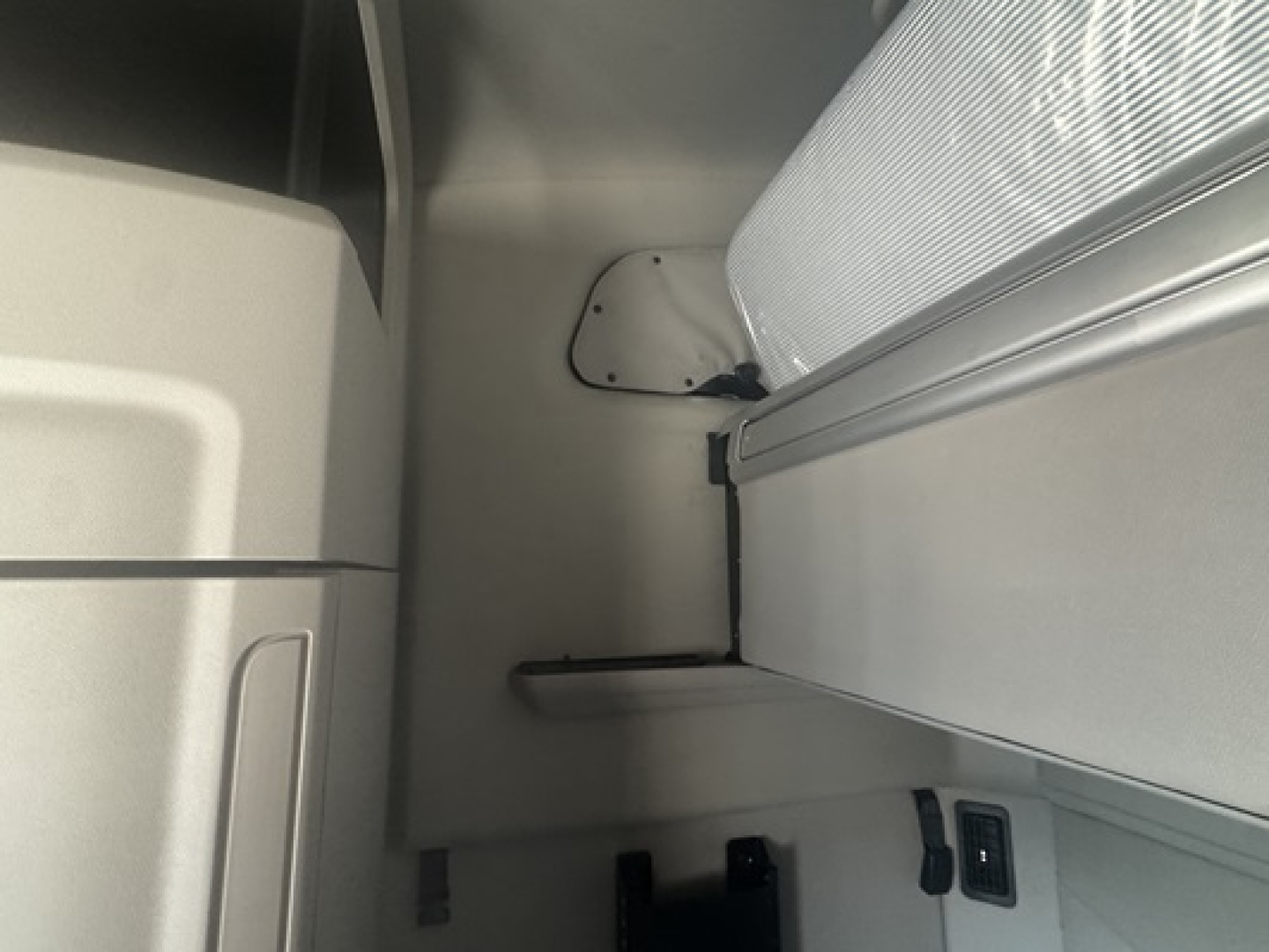 Peterbilt 579 cab interior view showing sleeper area and side panel, with a small storage shelf and window mount.
