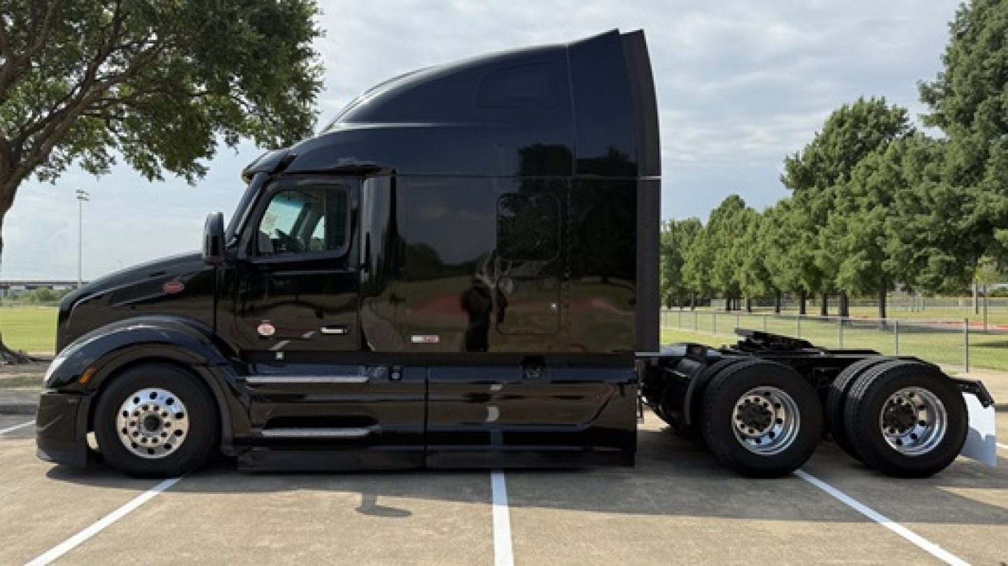 Peterbilt 579 tractor in black paint, side profile view with sleeper cab, three rear axles visible, daytime outdoor lot