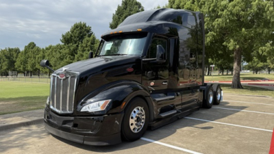 Peterbilt 579 day cab with glossy black paint, sleeper cab visible, chrome grille, dual rear axles, front view in a parking lot.