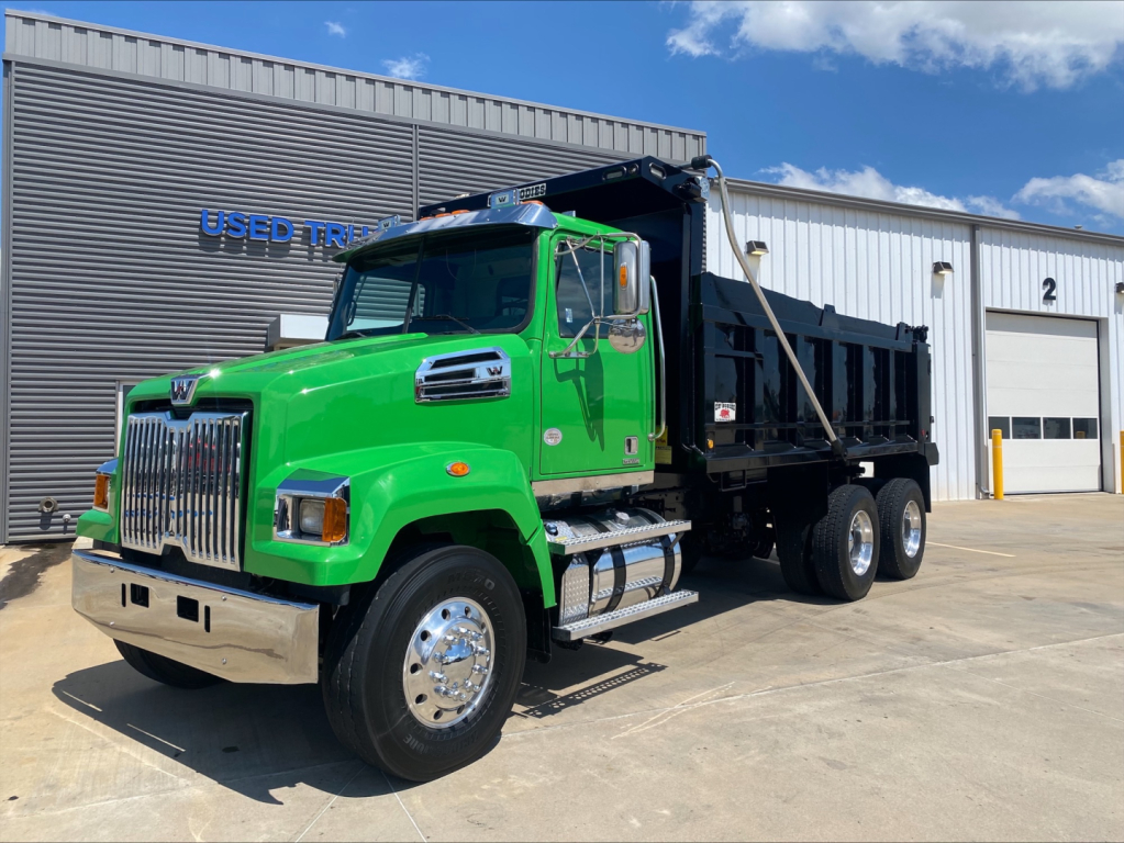 Green 2018 Western Star 4700SF dump truck with black dump bed, chrome bumper, and dual rear axles parked outside a service bay.