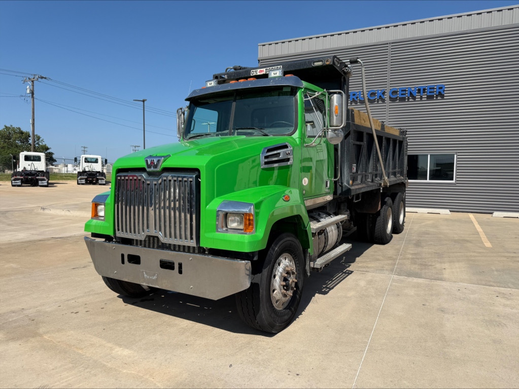 Western Star 4700SF dump truck front-left view showing bright green cab and black dump body in a dealership lot.