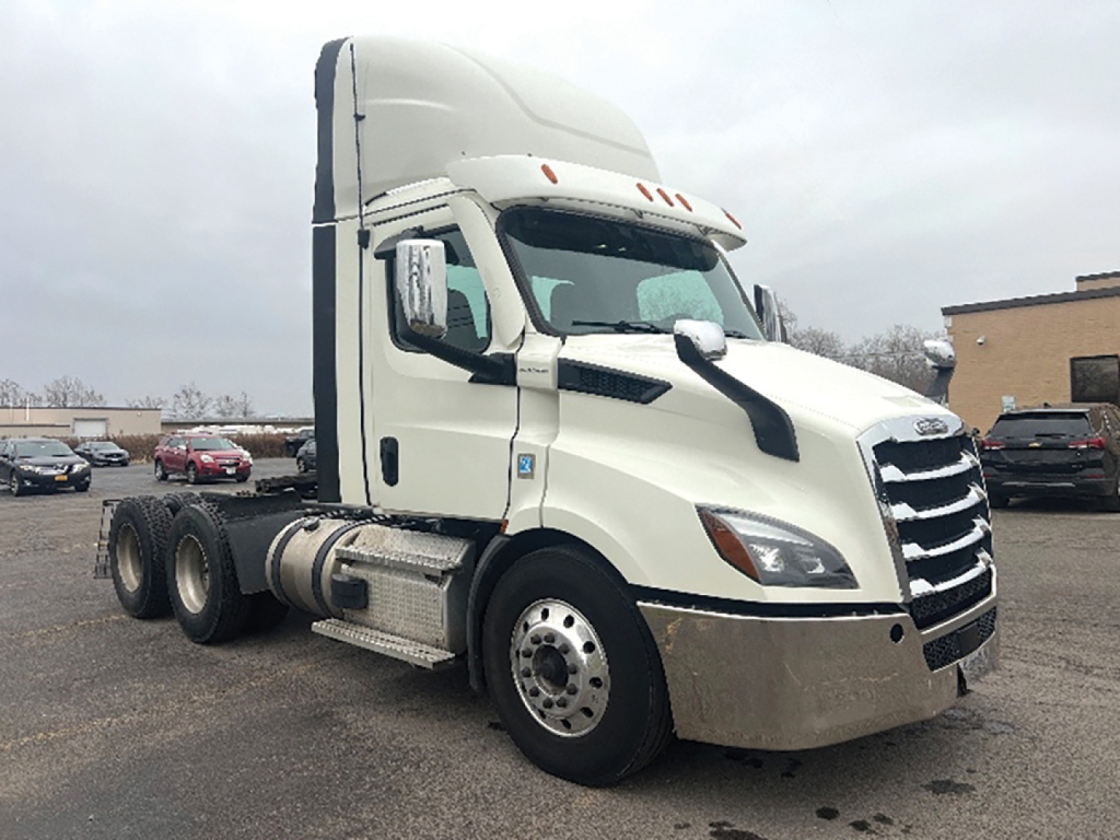 Truck in a parking lot: 2021 Freightliner Cascadia126 day cab tractor with large chrome grille, white cab, black accents, and dual rear axles.