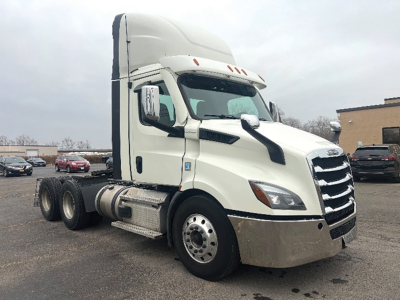 Truck in a parking lot: 2021 Freightliner Cascadia126 day cab tractor with large chrome grille, white cab, black accents, and dual rear axles.