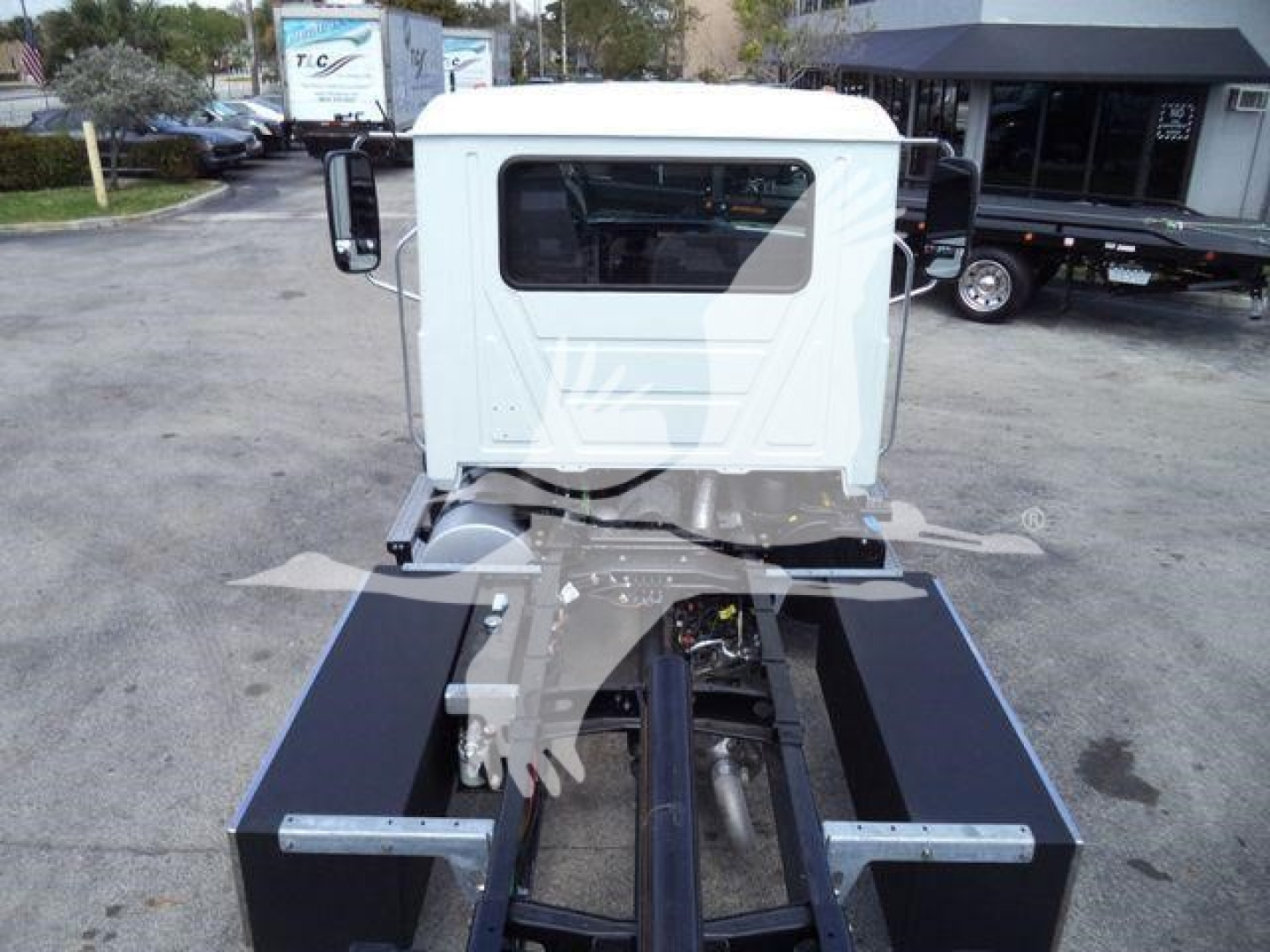 Truck cab and chassis of a new 2027 Mack MD6 rollback with a white cab and dark blue chassis rails, seen from rear perspective.