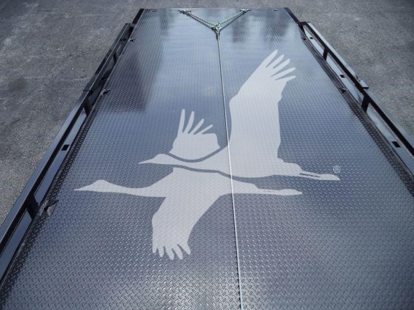Flatbed truck ramp with diamond plate surface featuring a large white geese artwork in flight.
