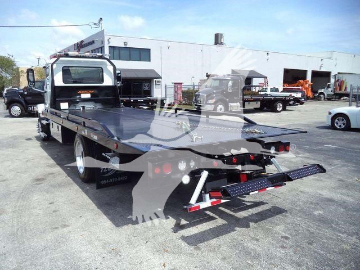 MD6 Mack rollback truck flatbed in a dealership lot, rear view showing loading ramps and deck with reflective lights