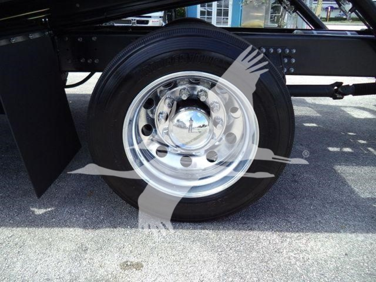 Rear wheel and heavy-duty chrome hub on Mack MD6 truck chassis showing polished steel wheel and tire, with frame and mud flap nearby.