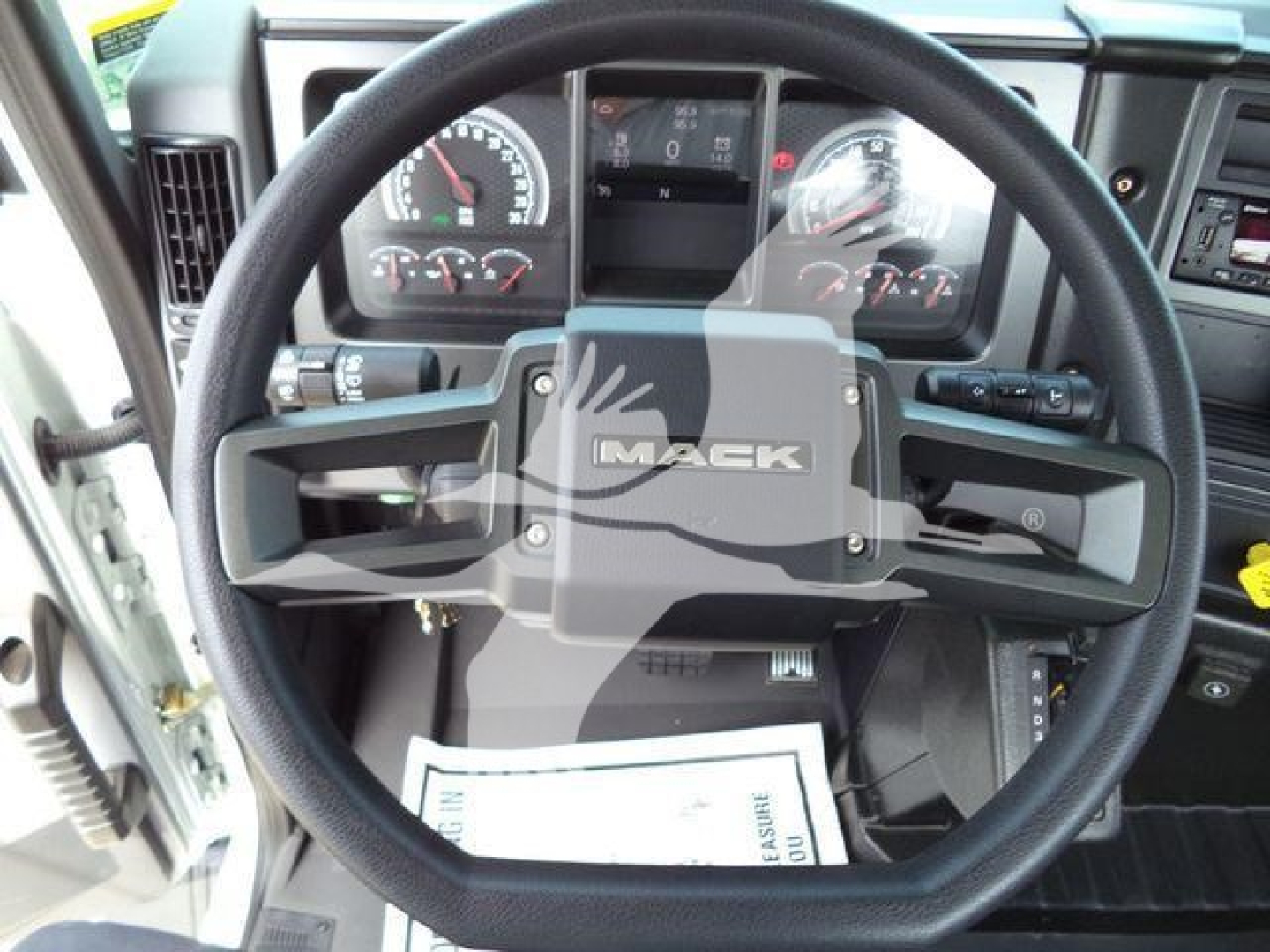 Steering wheel and dashboard of a Mack MD6 truck cab showing the Mack emblem; instrument cluster with gauges and a center display.