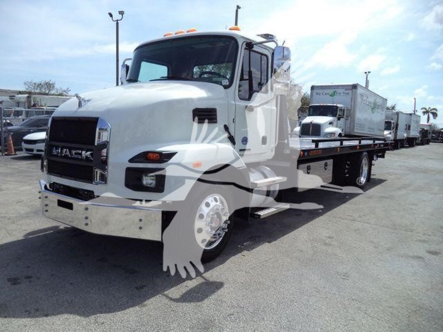 Mack MD6 roll-off truck in white, side view showing front grille, cab, and flatbed with a container at the rear; clear daytime lot with other trucks in background.